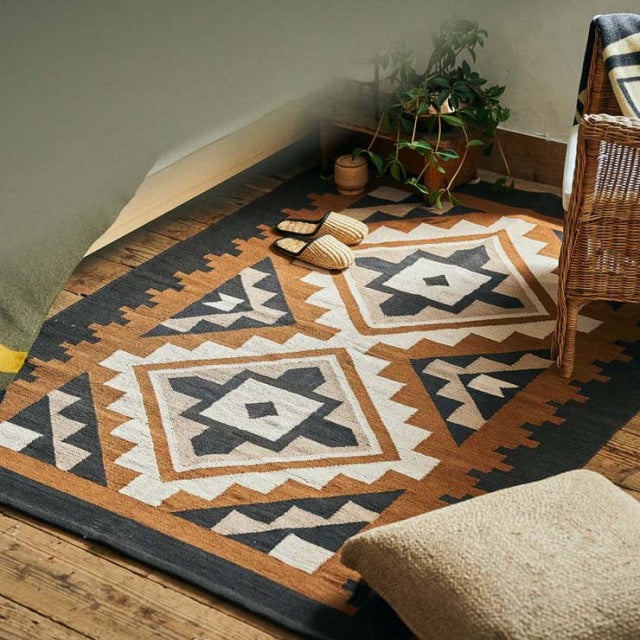 Mid-century vintage cotton rug with geometric patterns in beige, black, and rust, styled on teak wood floor with wicker.