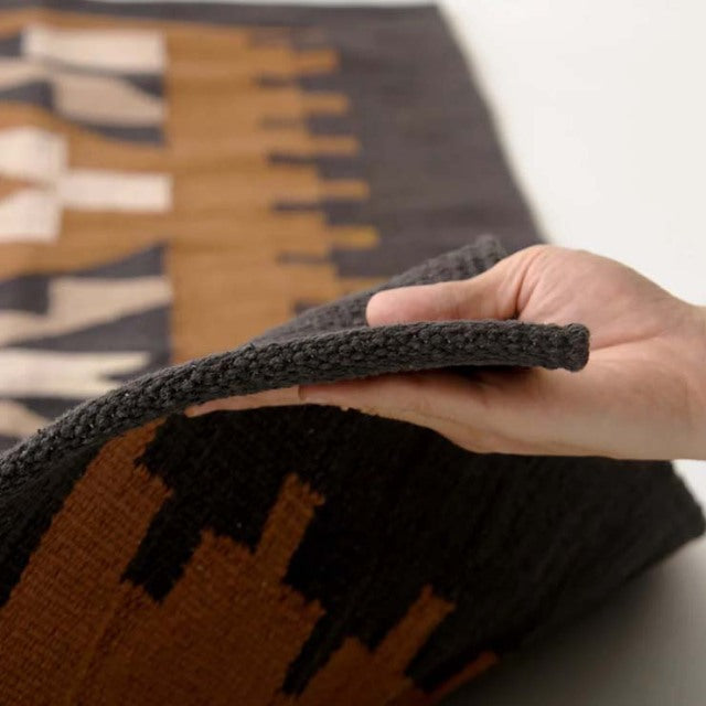 Close-up of a thick vintage cotton rug with geometric patterns in black, brown, and beige tones, showcasing a textured weave .