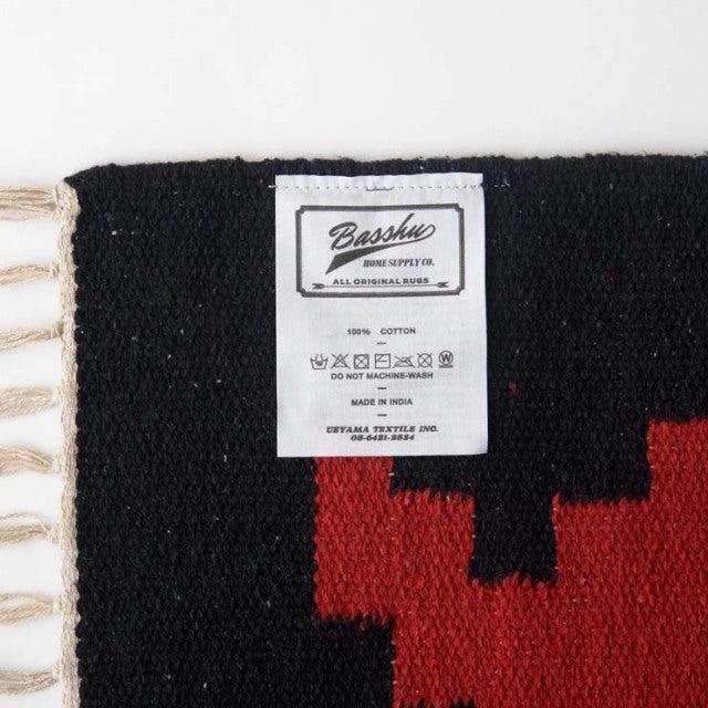 Close-up of Basshu cotton rug label on black and red woven fabric with fringed edge, vintage British design.