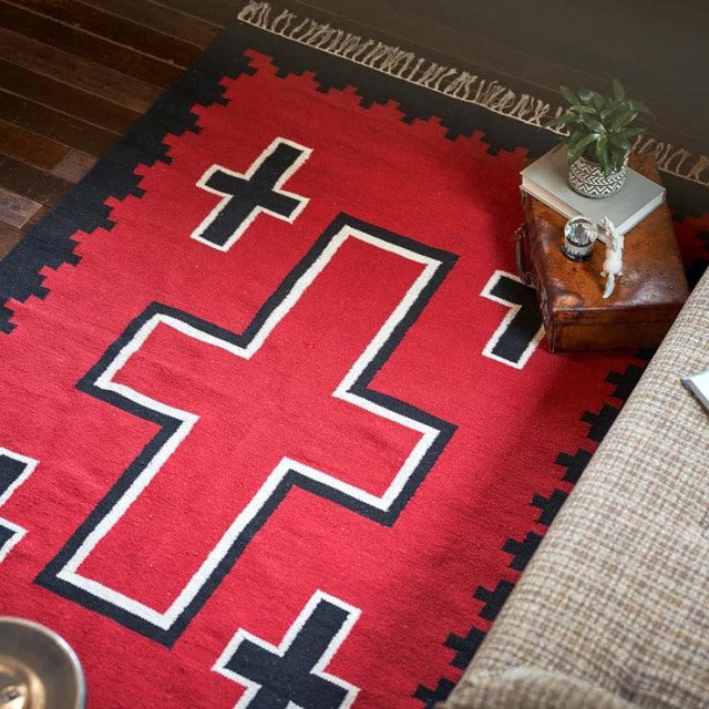 Red vintage cotton rug with bold black and white geometric crosses, paired with mid-century teak side table featuring rich.