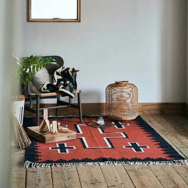 Vintage teak mid-century chair with curved backrest on a red and black British cotton rug with geometric patterns and tassel .