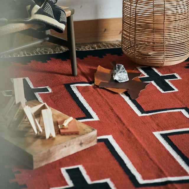 Vintage teak mid-century table leg on vibrant red British cotton rug with bold geometric patterns, natural wood grain visible.