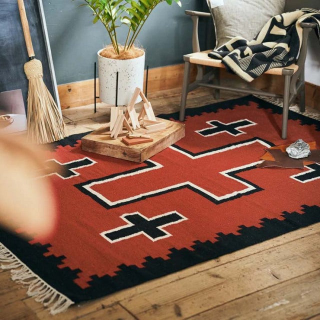 Vintage cotton rug with bold black and rust geometric patterns, fringed edges on natural wood floor beneath mid-century teak .