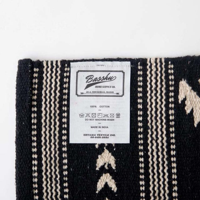 Black and beige vintage cotton rug label with Basshu brand and care instructions, textured woven fabric visible.