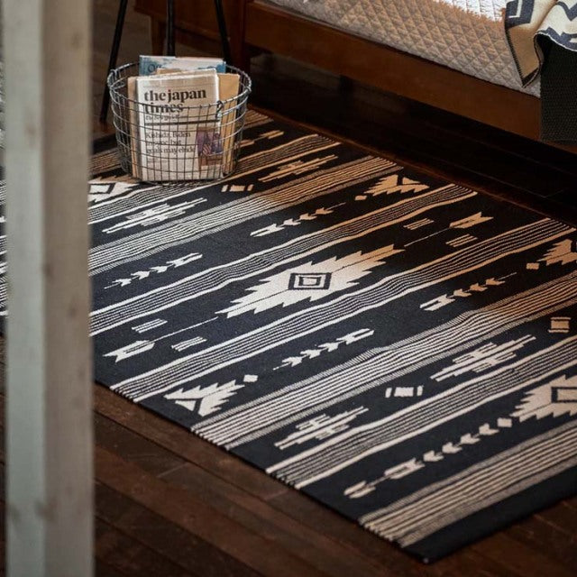 Black and white vintage cotton rug with geometric patterns placed under a mid-century teak wooden furniture leg with visible .