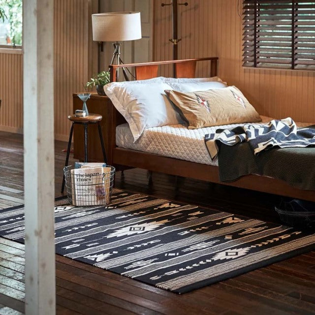 Mid-century teak daybed with clean lines and visible wood grain, styled with white and beige cushions, set on a dark.