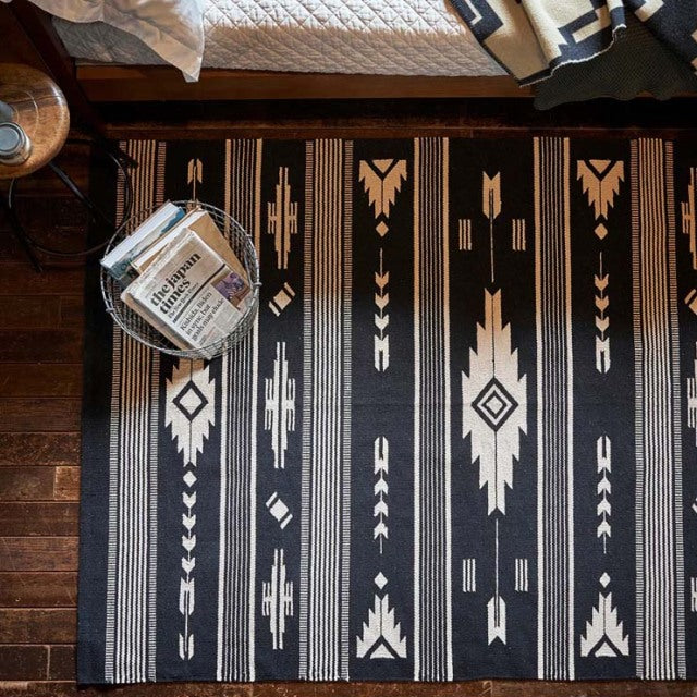 Mid-century British vintage rug with bold white geometric patterns on black, laid on dark teak floor.