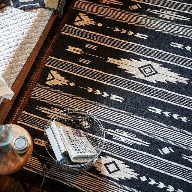 Black and beige vintage-style cotton rug with geometric patterns on teak mid-century British furniture floor.