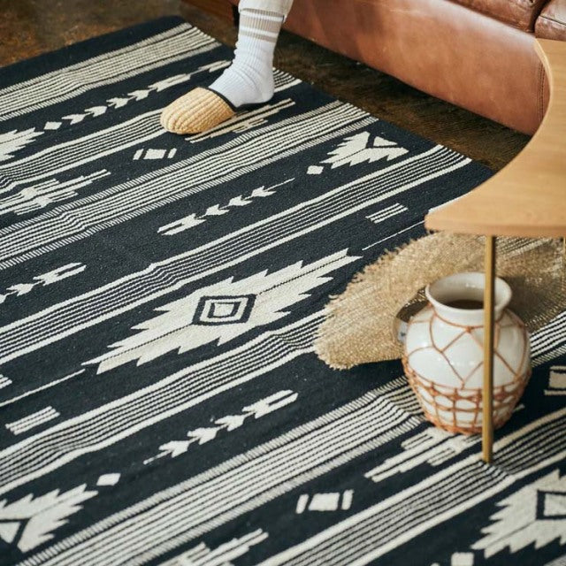 Vintage black and white cotton rug with geometric patterns on teak mid-century British furniture floor.