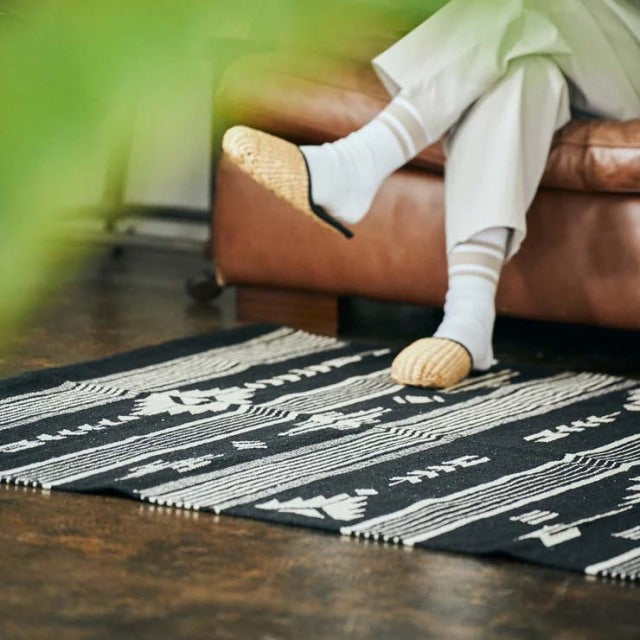 Black and white vintage cotton rug with geometric patterns, laid on dark wooden floor near mid-century teak British-style.