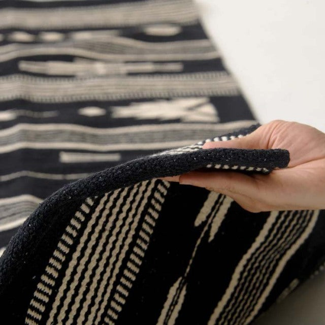 Black and white vintage cotton rug with bold geometric stripes, thick textured weave, flexible edge held up by hand.