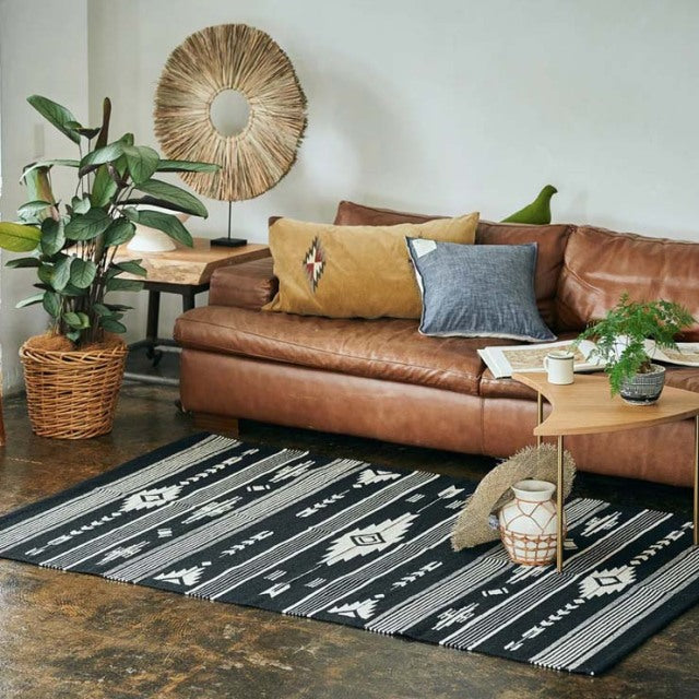 Mid-century British teak coffee table with sleek angled legs on a black and white vintage cotton rug with geometric.