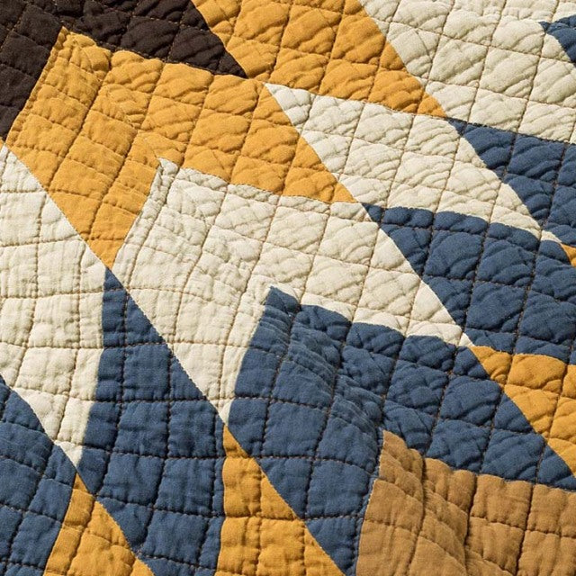 Patchwork quilt cover with geometric design in camel, navy, cream, and mustard, featuring textured stitching and vintage.