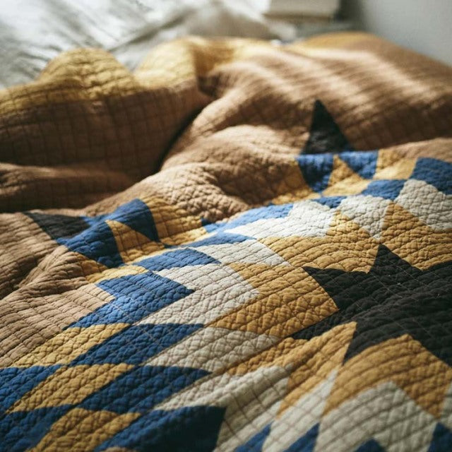 Camel patchwork quilt with vintage British mid-century design, featuring geometric patterns in blue, cream, and black tones.