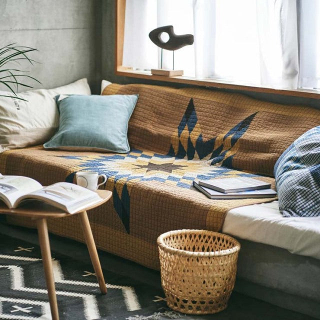 Mid-century British teak sofa with visible wood grain, covered by a camel patchwork quilt, styled with blue and white.