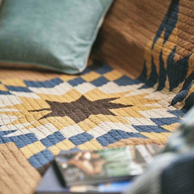 Patchwork quilt cover in camel tones with blue and brown geometric vintage pattern, styled on teak mid-century British.