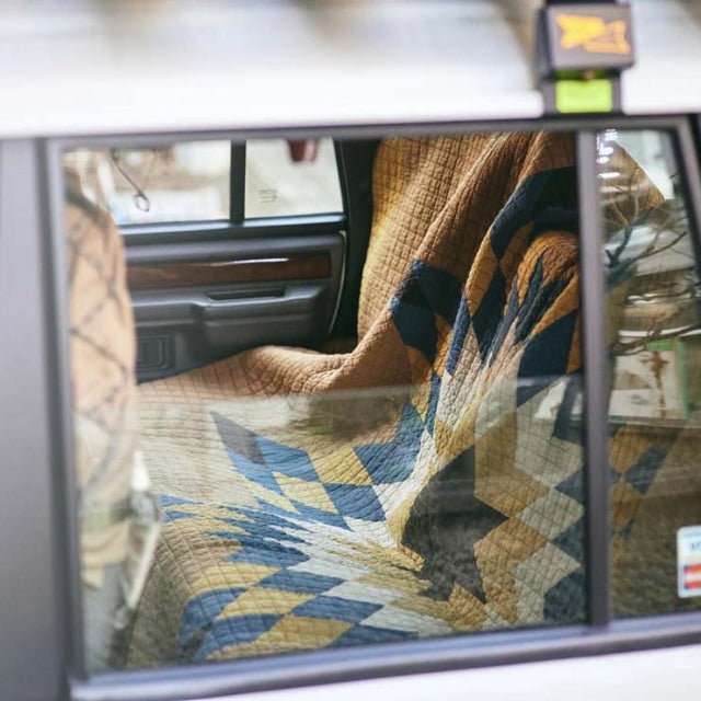 British mid-century vintage teak car interior with polished wood grain and a camel patchwork quilt draped over the seat.