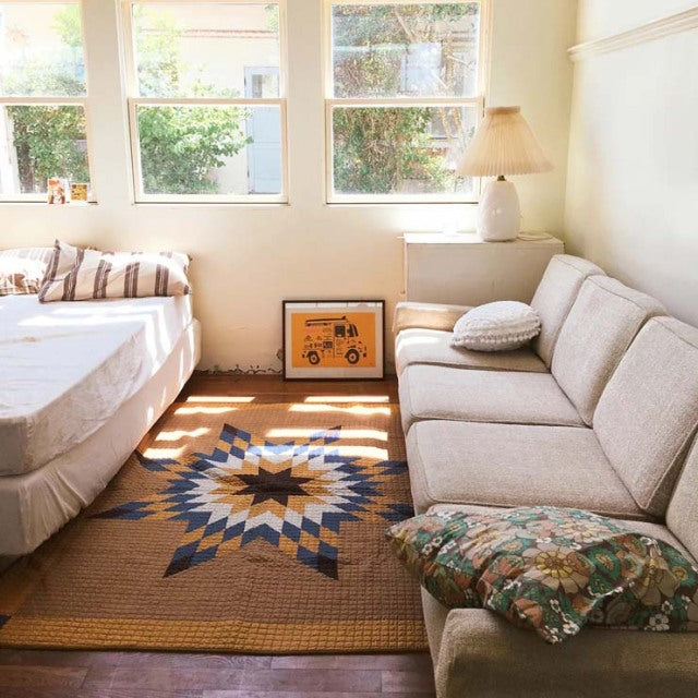 Mid-century British vintage teak sofa with tapered legs and beige upholstery beside a light wood bed, set on a geometric.