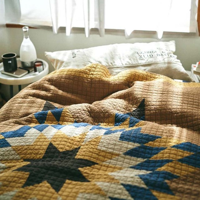 Vintage patchwork quilt cover in camel tones with blue star pattern, soft textured cotton fabric on mid-century British teak .