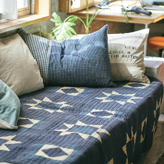 Blue patchwork quilt cover with vintage British mid-century pattern, laid over teak furniture with clean lines and visible.