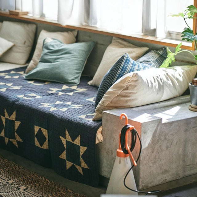 Mid-century teak sofa with visible wood grain, covered by a blue patchwork quilt featuring star patterns, styled with beige.