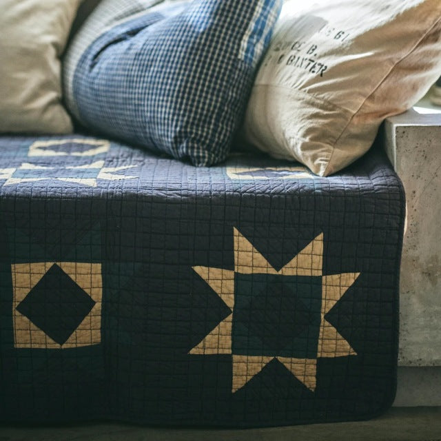 Blue patchwork quilt cover with beige star and diamond patterns on mid-century teak furniture.