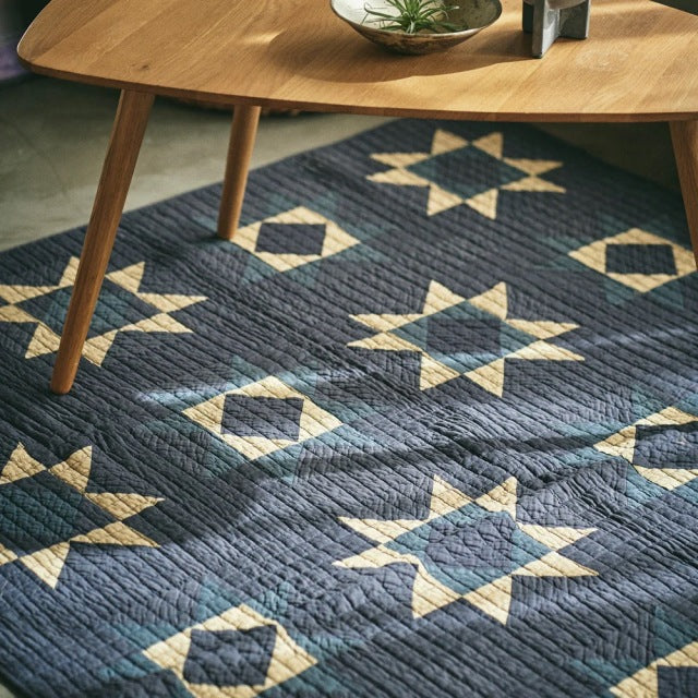 Mid-century teak coffee table with tapered legs on blue vintage patchwork quilt featuring geometric star patterns.