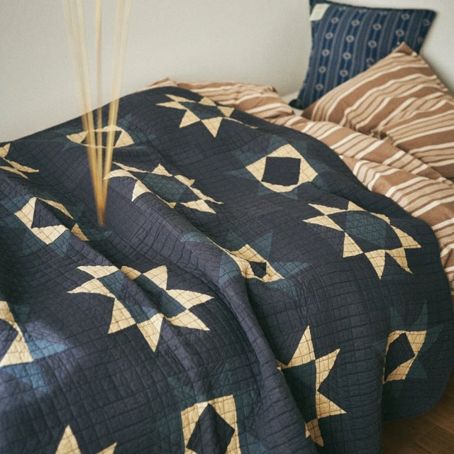 Vintage British mid-century teak bed frame with visible wood grain and tapered legs, topped with a blue patchwork quilt.