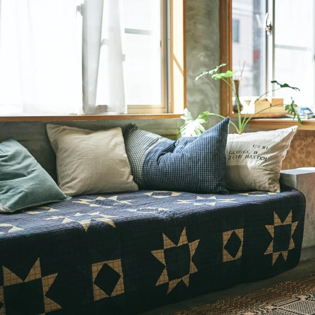 Mid-century British vintage teak sofa with clean lines, featuring dark blue patchwork quilt cover with geometric patterns.