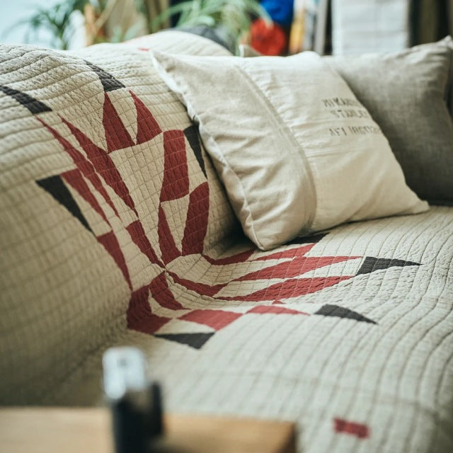Beige patchwork quilt cover with vintage-inspired red and brown geometric patterns on a mid-century teak sofa, featuring.