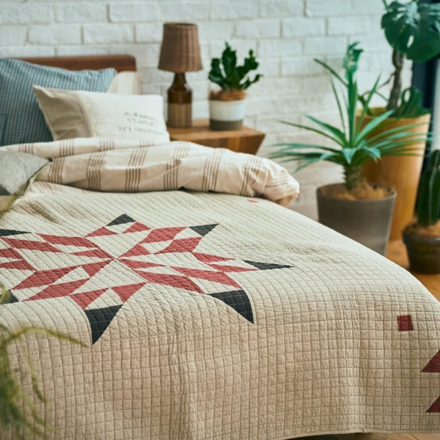 Beige patchwork quilt cover with vintage-inspired geometric patterns in red, black, and green, styled on mid-century teak.