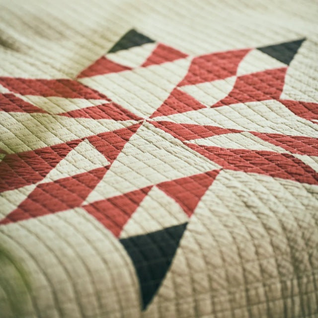 Patchwork quilt cover with beige base and red, black geometric vintage pattern, textured stitching visible.