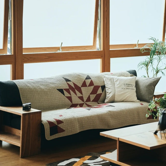 Mid-century British vintage teak sofa with visible wood grain, clean lines, and a beige patchwork quilt featuring red star.
