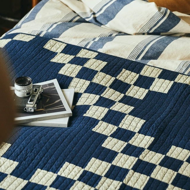 Navy and cream British vintage patchwork quilt cover with textured stitching, styled over teak mid-century furniture surface .