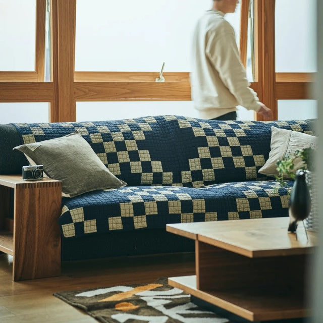 Mid-century British teak sofa with clean lines covered in a navy patchwork quilt, accented by soft gray pillows and a solid.