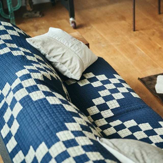 Navy blue and white patchwork quilt cover with vintage British mid-century teak sofa featuring visible wood grain and.