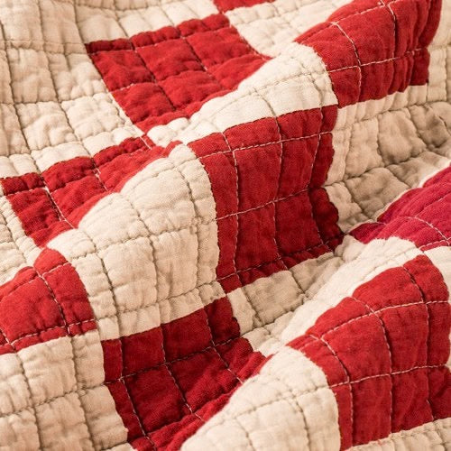 Red and beige patchwork quilt cover with visible hand-stitched details, reflecting vintage British textile craftsmanship.