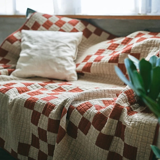 Red and beige patchwork quilt draped over teak mid-century British vintage furniture with visible wood grain and clean lines.