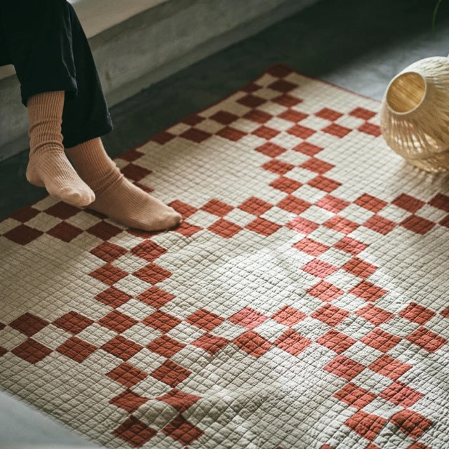 Mid-century British vintage patchwork quilt cover in red and cream, textured woven fabric with geometric design, draped on.