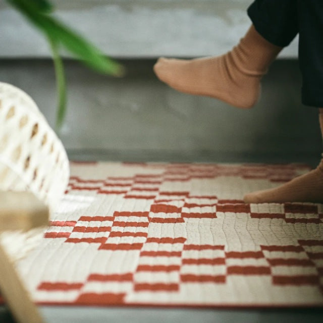 Mid-century British patchwork quilt cover in red and beige with textured stitching on wooden floor, feet stepping on edge.