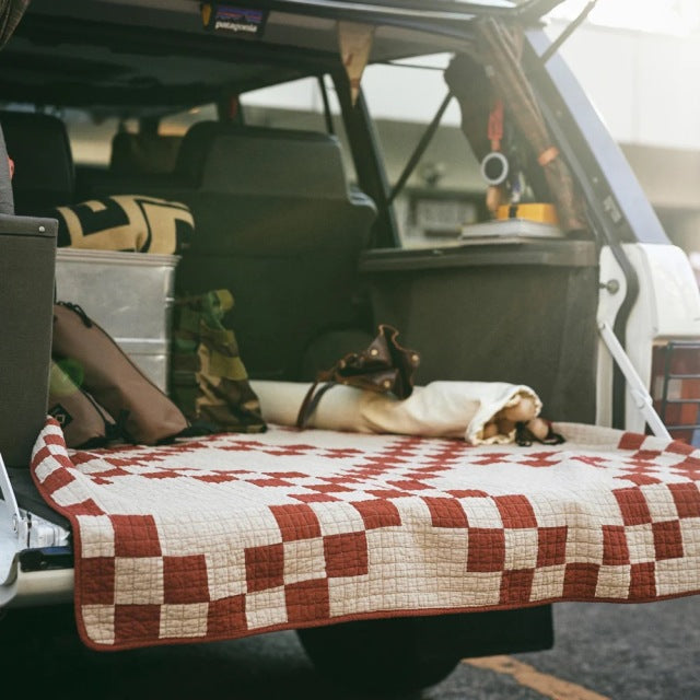 Vintage teak mid-century British patchwork quilt cover in red and cream draped over car tailgate with dog resting on it and.