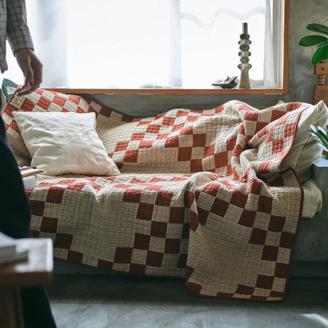 Mid-century British vintage teak sofa with square legs, draped with red and beige patchwork quilt cover featuring geometric.