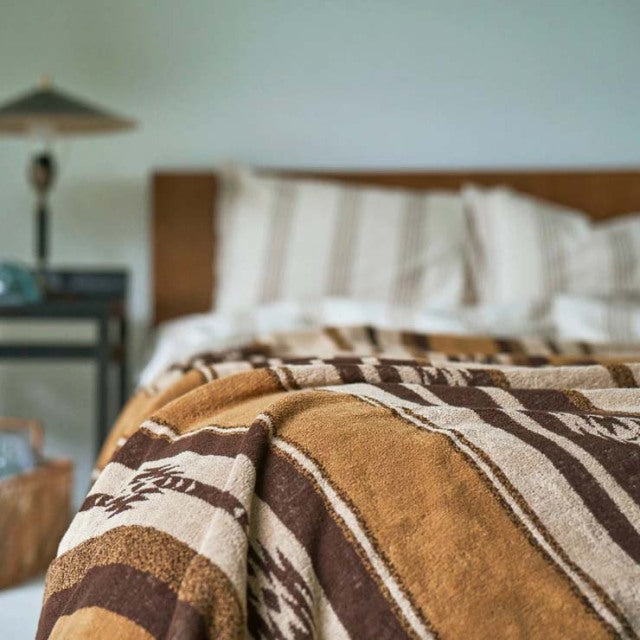 Brown and cream cotton pile blanket with native border draped over teak mid-century bed frame in British vintage style.