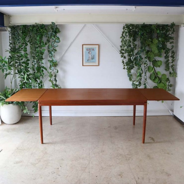 Vintage mid-century teak dining table by Johannes Andersen with clean rectangular top, slender tapered legs, and warm wood.