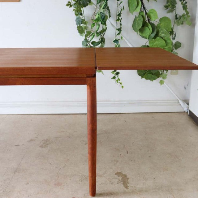 Mid-century vintage teak dining table by Johannes Andersen with sleek tapered legs and rich wood grain, extending leaf open.
