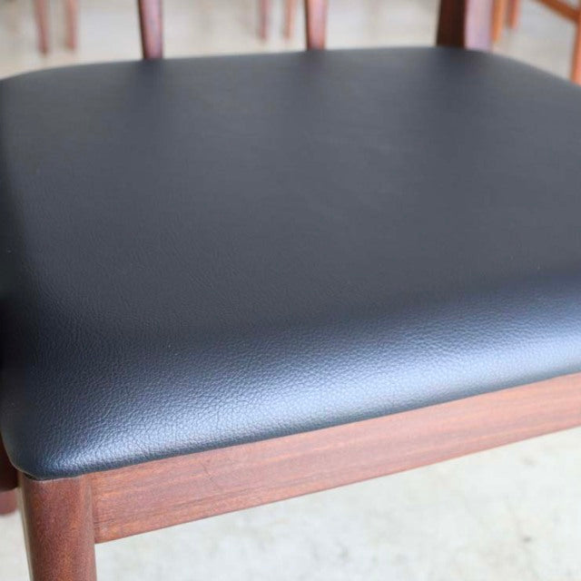 Mid-century vintage British teak dining chair seat with smooth black leather cushion and visible wood grain.