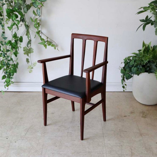 Vintage teak dining chair with armrests, British mid-century design by John Herbert, sleek wood grain and black upholstered.