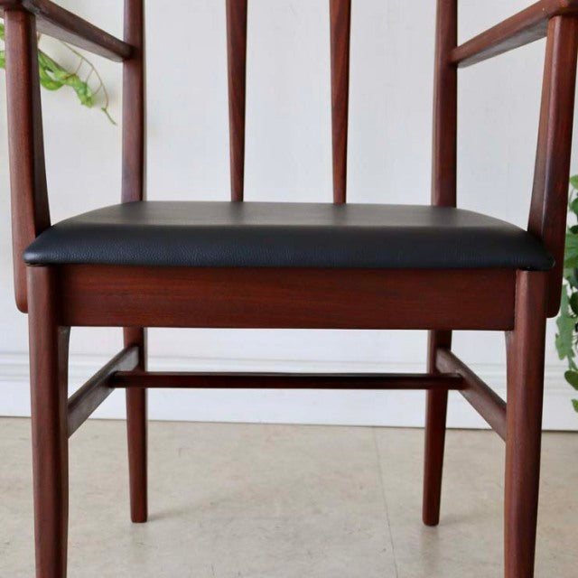 Mid-century British vintage teak dining chair with armrests, black cushioned seat, slender legs, and vertical slat back.