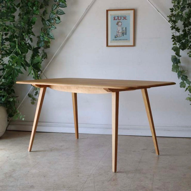 Mid-century British Ercol dining table in light teak with tapered legs and smooth wood grain surface, vintage Danish design.