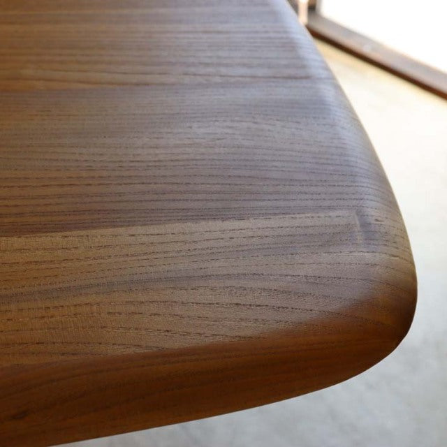 Close-up of vintage British mid-century Ercol dining table corner in smooth teak wood with visible grain and rounded edge.